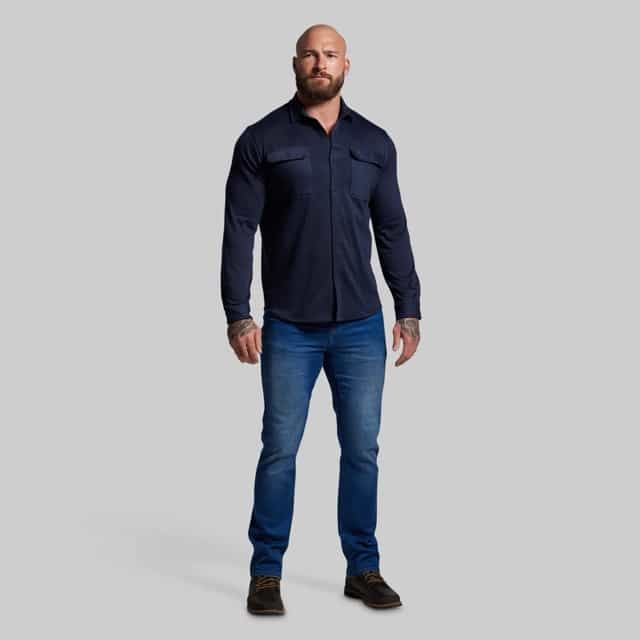 Man wearing a navy long-sleeve shirt and blue jeans on a gray background