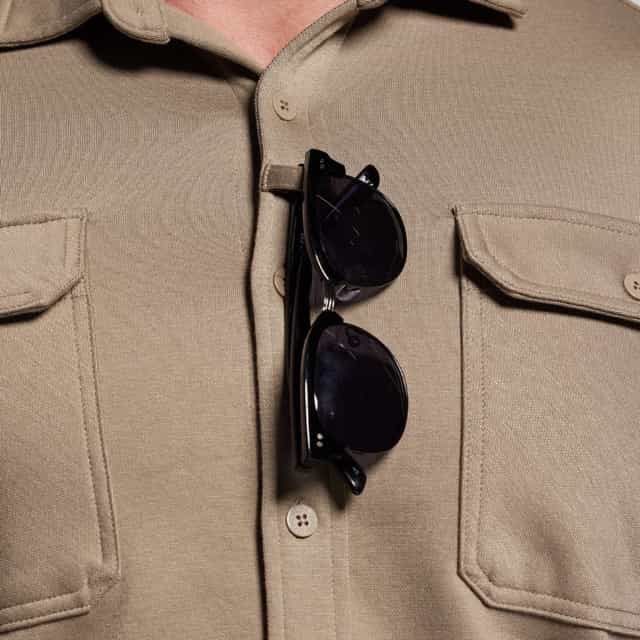 Black sunglasses hanging from a beige shirt collar