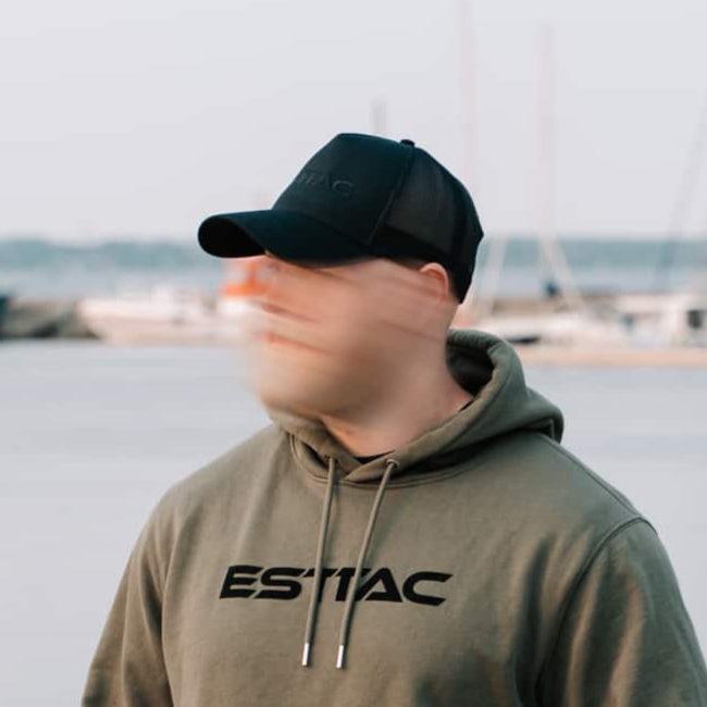 Person wearing a green hoodie with 'ESTTAC' logo by a waterfront