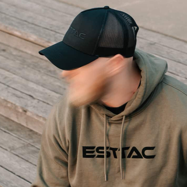 Person wearing a green hoodie with 'ESTTAC' logo sitting on a wooden deck.