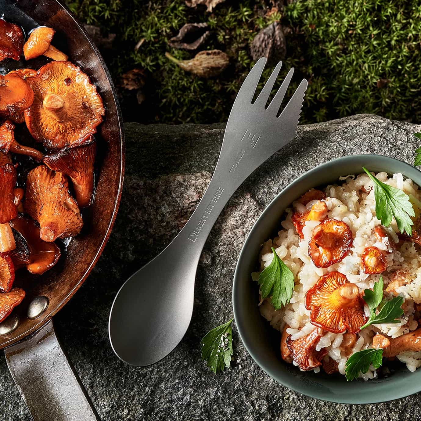 Light My Fire Swedish Spork Titanium on a stone surface with a bowl of food and pan of mushrooms.