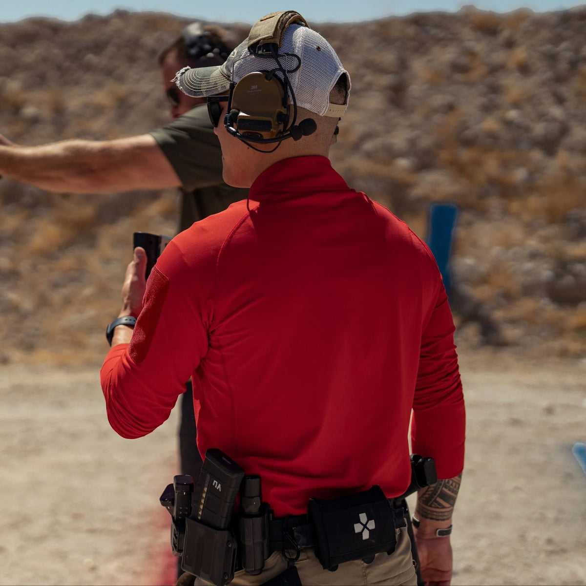 Vertx Men's Enduro Training Long Sleeve Shirt in red at an outdoor shooting range, back view