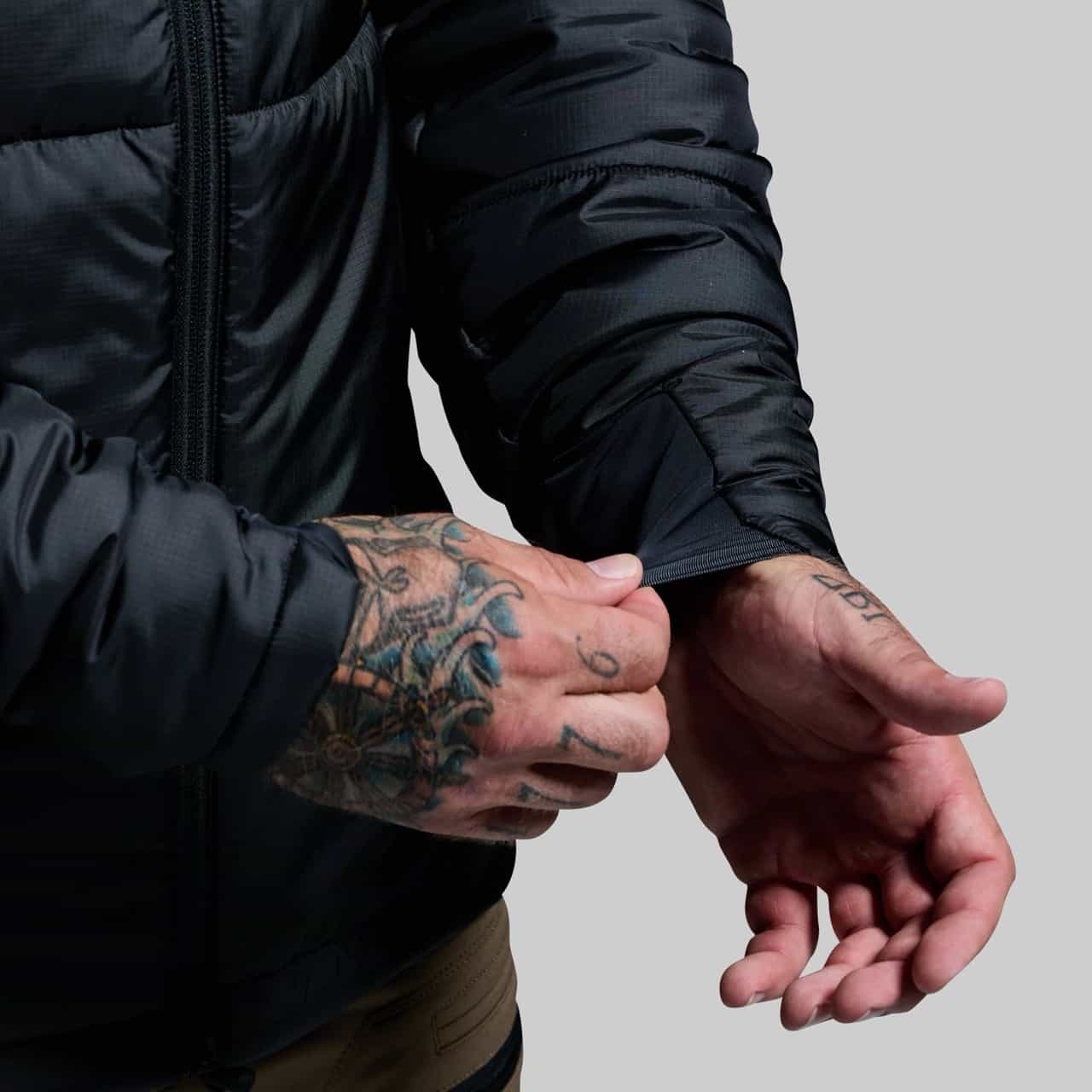 Person wearing a black jacket with tattooed hands on a plain background