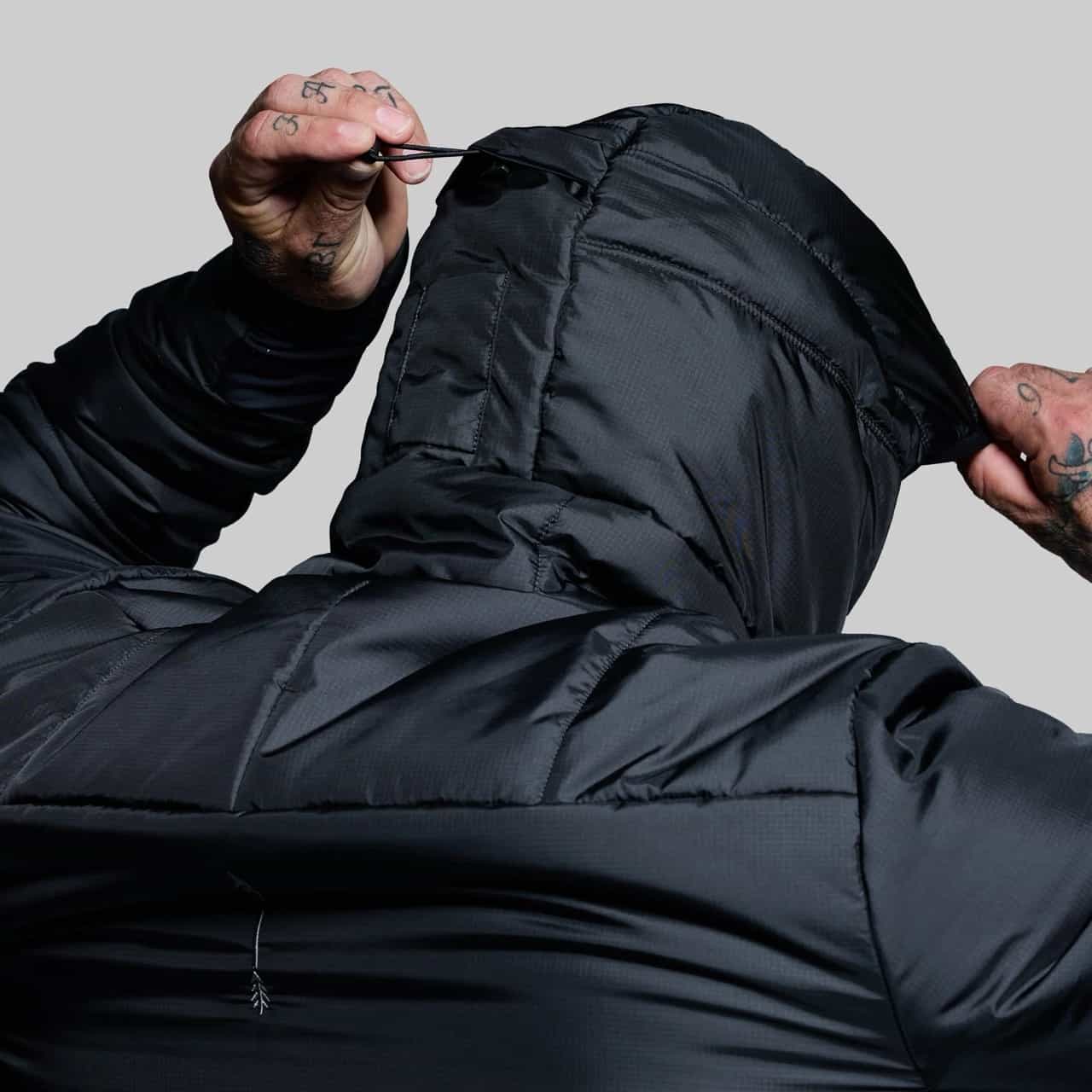 Person wearing a black puffer jacket with the hood up against a gray background