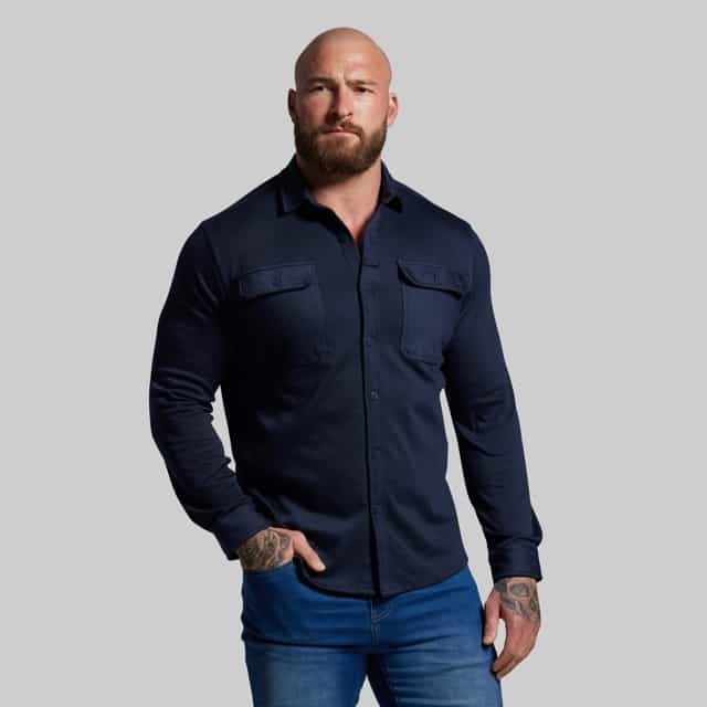 Man wearing a navy blue shirt and blue jeans against a gray background