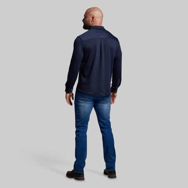 Man wearing a navy long-sleeve shirt and blue jeans on a light gray background