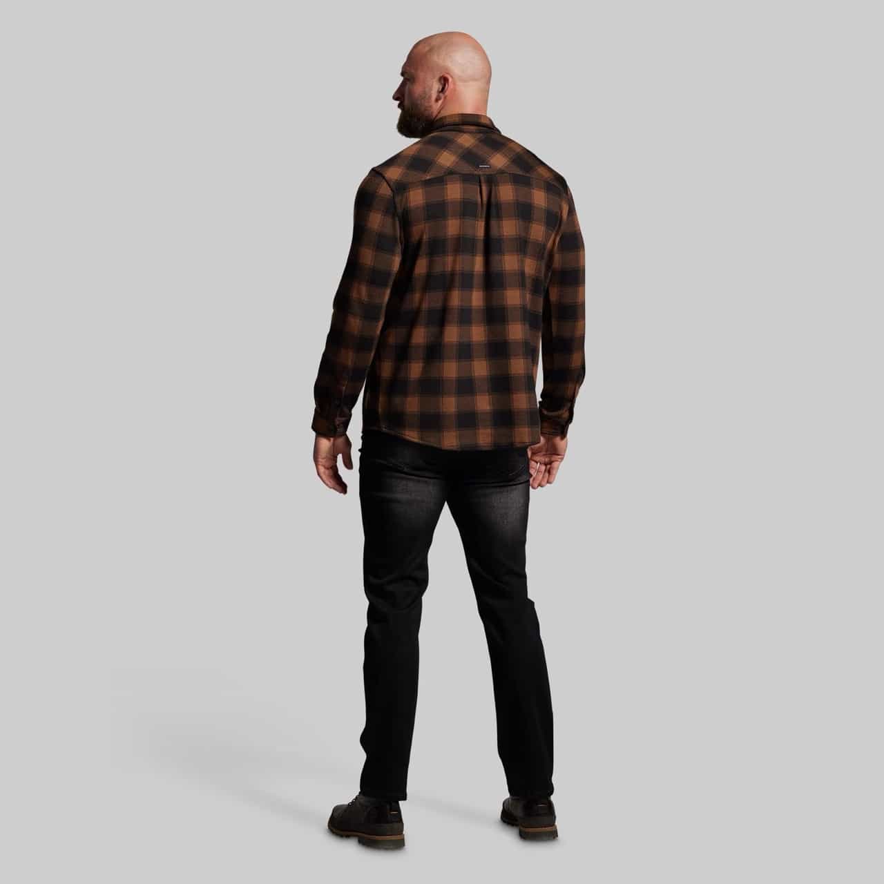 Man wearing a brown and black plaid shirt and dark jeans on a gray background