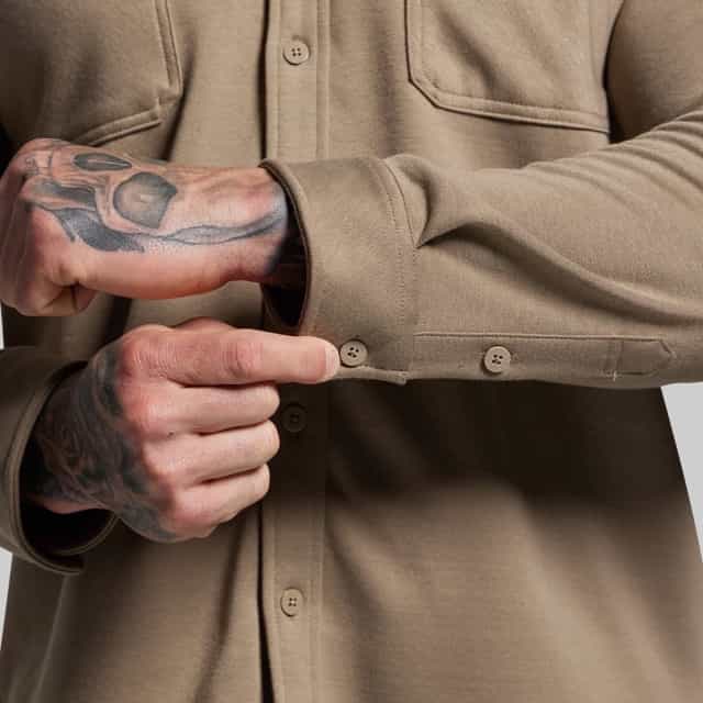 Person wearing a brown shirt with tattooed arms pointing to a button