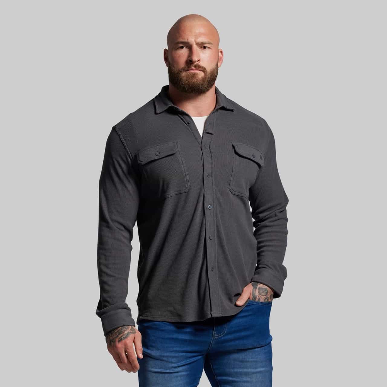 Man wearing a dark gray button-up shirt and blue jeans against a plain background