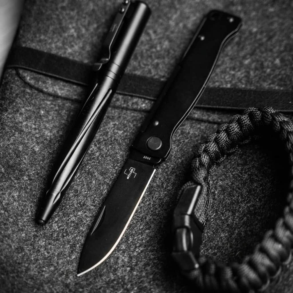 Böker Plus Atlas All Black pocket foldable knive and pen on a textured surface with a rope